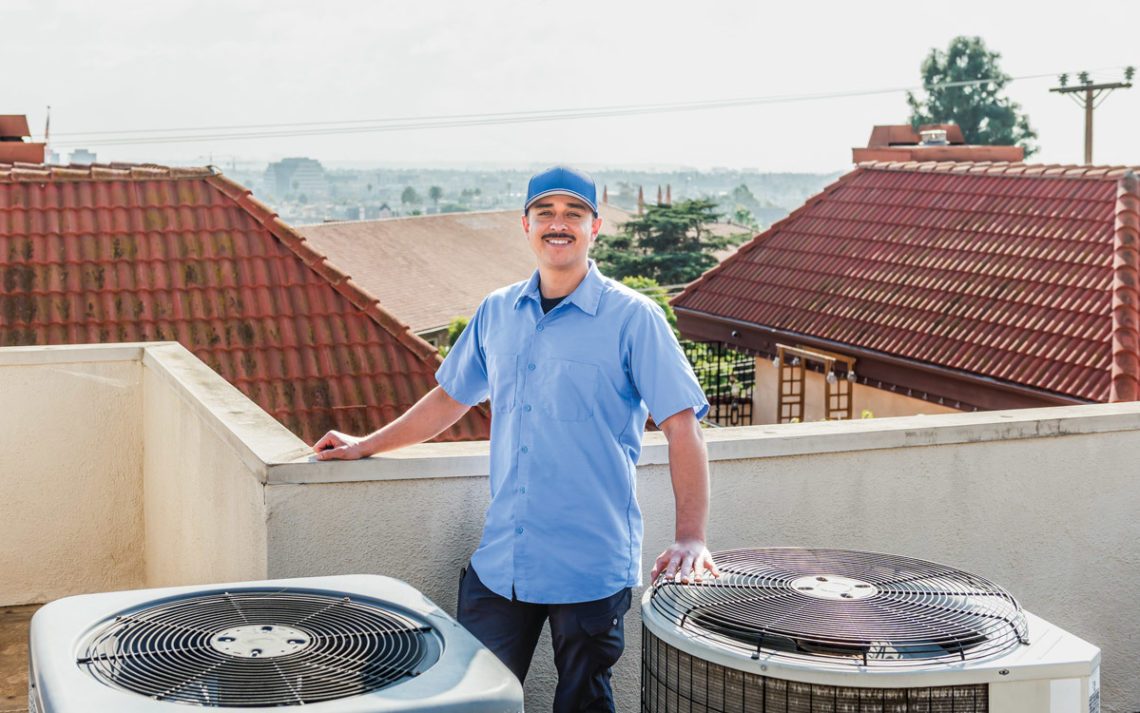 John Castillo, owner of 310 HVAC, standing on a rooftop beside two commercial air conditioning units